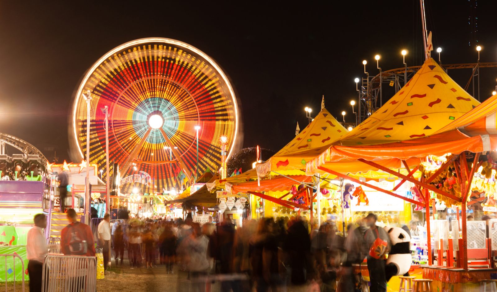 A lit-up Ferris wheel and striped food tents on a busy fair midway at night