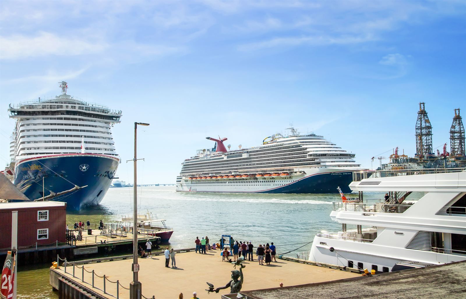 Two large cruise ships docked at the Port of Galveston, with people walking on a waterfront plaza